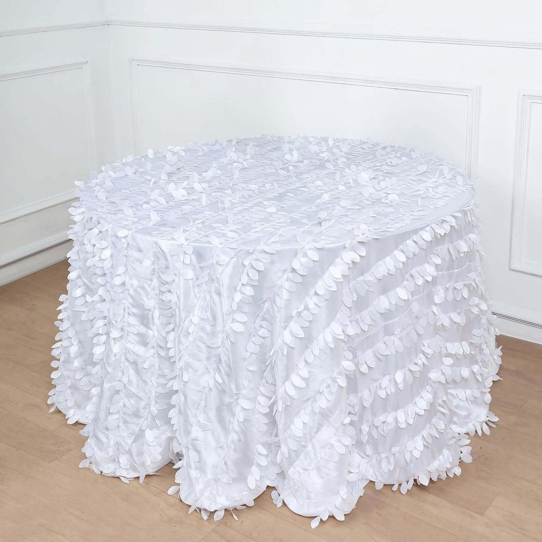 White tablecloth with leaf design draping over a round table.