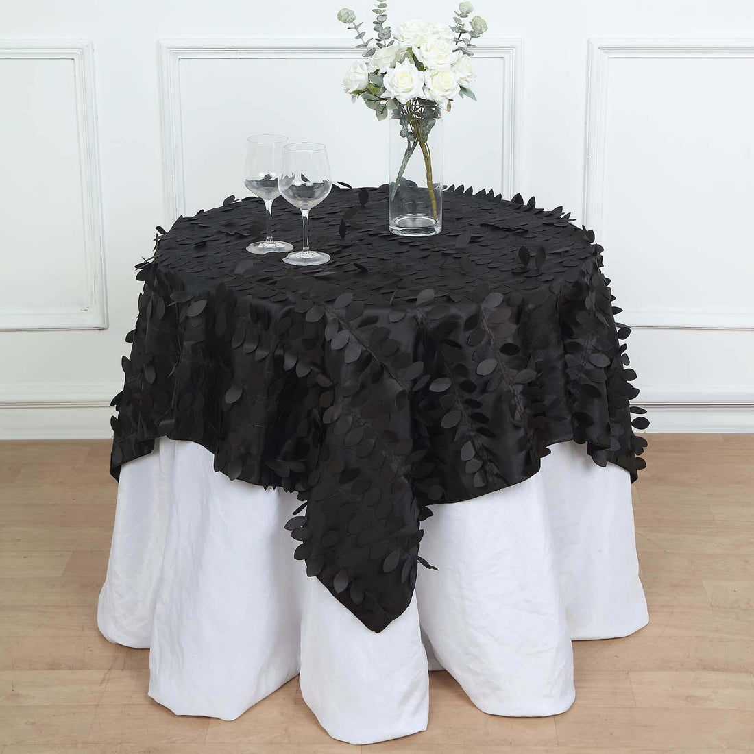 Black tablecloth with leaf design draped over a white table in a styled setting.
