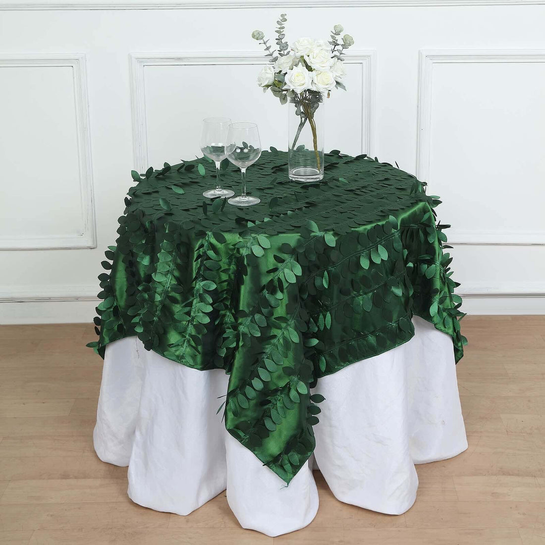 Green leaf tablecloth on a white table with glasses and a floral centerpiece.
