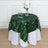 Green leaf tablecloth on a white table with glasses and a floral centerpiece.