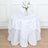 White tablecloth with leaf design draped over a round table with glasses and flowers.