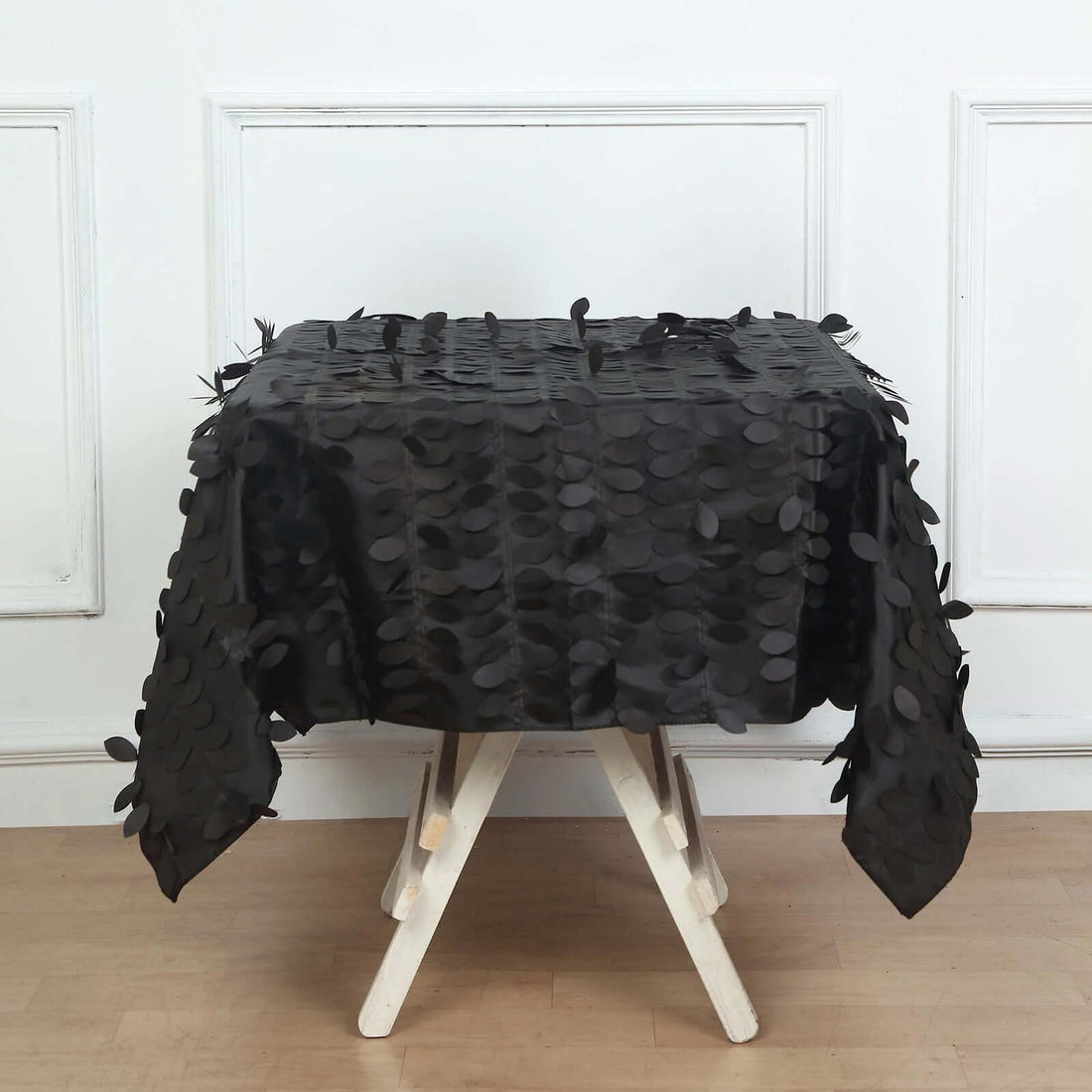 Black textured tablecloth with leaf embellishments on a wooden table.