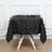 Black textured tablecloth with leaf embellishments on a wooden table.
