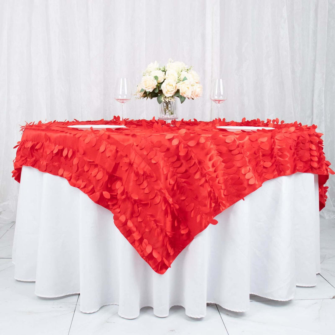 Red leaf-patterned tablecloth draped over a round table with floral centerpiece.