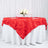 Red leaf-patterned tablecloth draped over a round table with floral centerpiece.