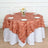 Round table with a peach leaf-patterned tablecloth and a floral centerpiece.
