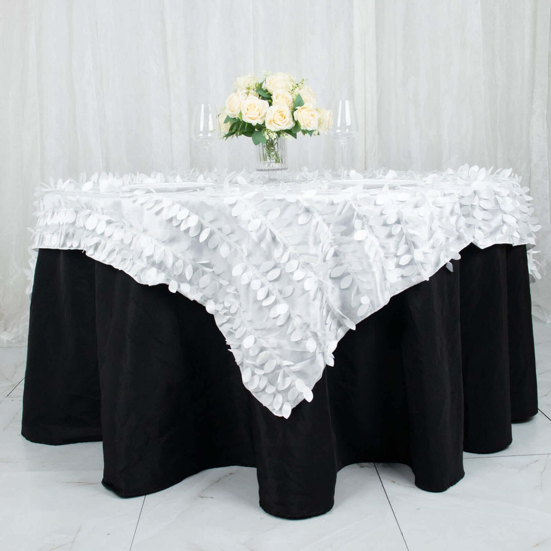 White floral tablecloth draped over a black table with a floral centerpiece.
