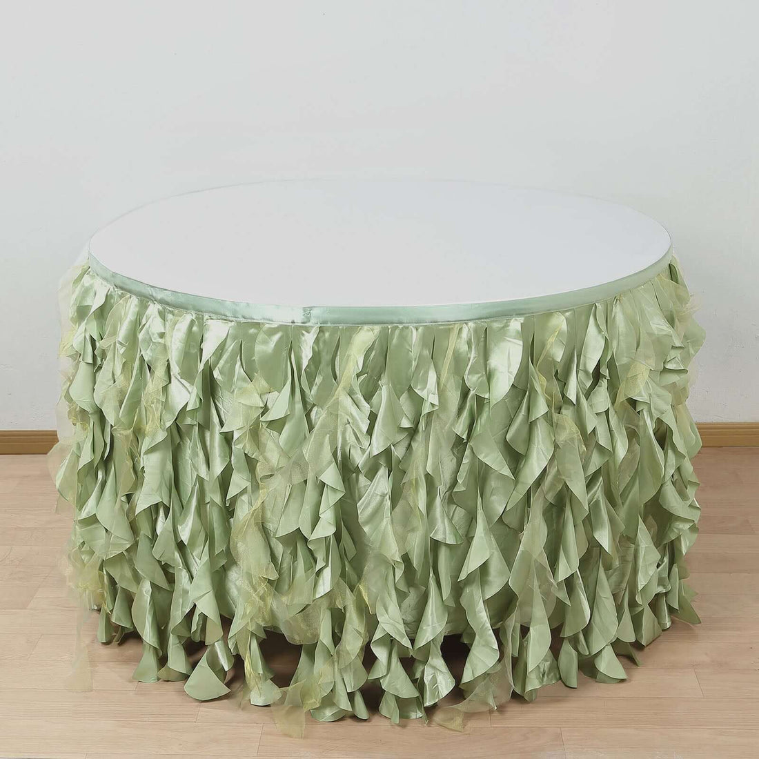 Round table with green ruffled table skirt on a plain background.
