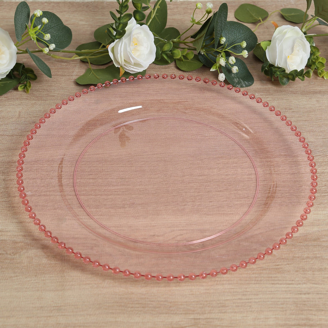 Pink glass plate with beaded rim on a wooden surface.