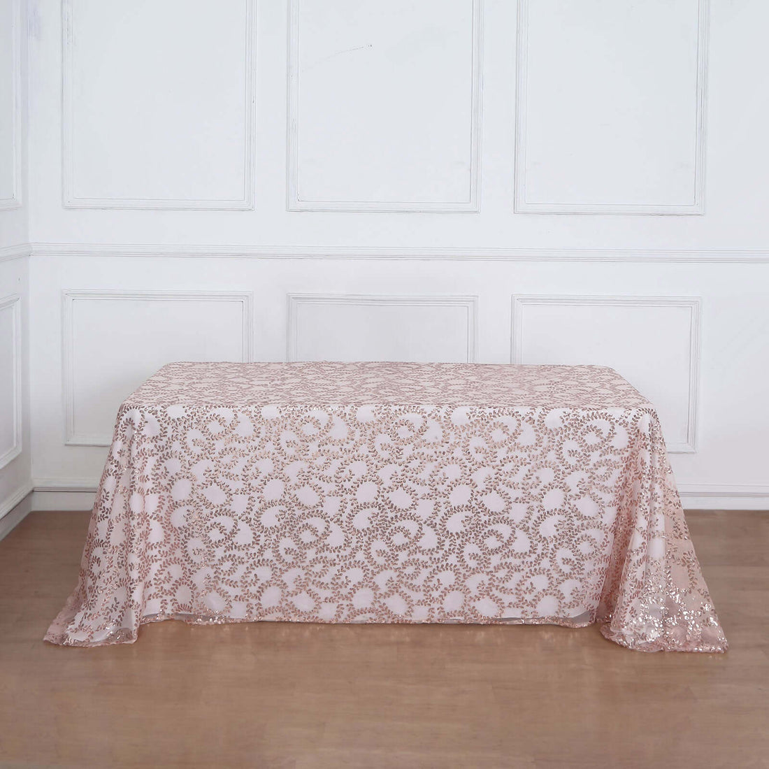 Rose gold sequin tablecloth with floral pattern on a wooden floor.