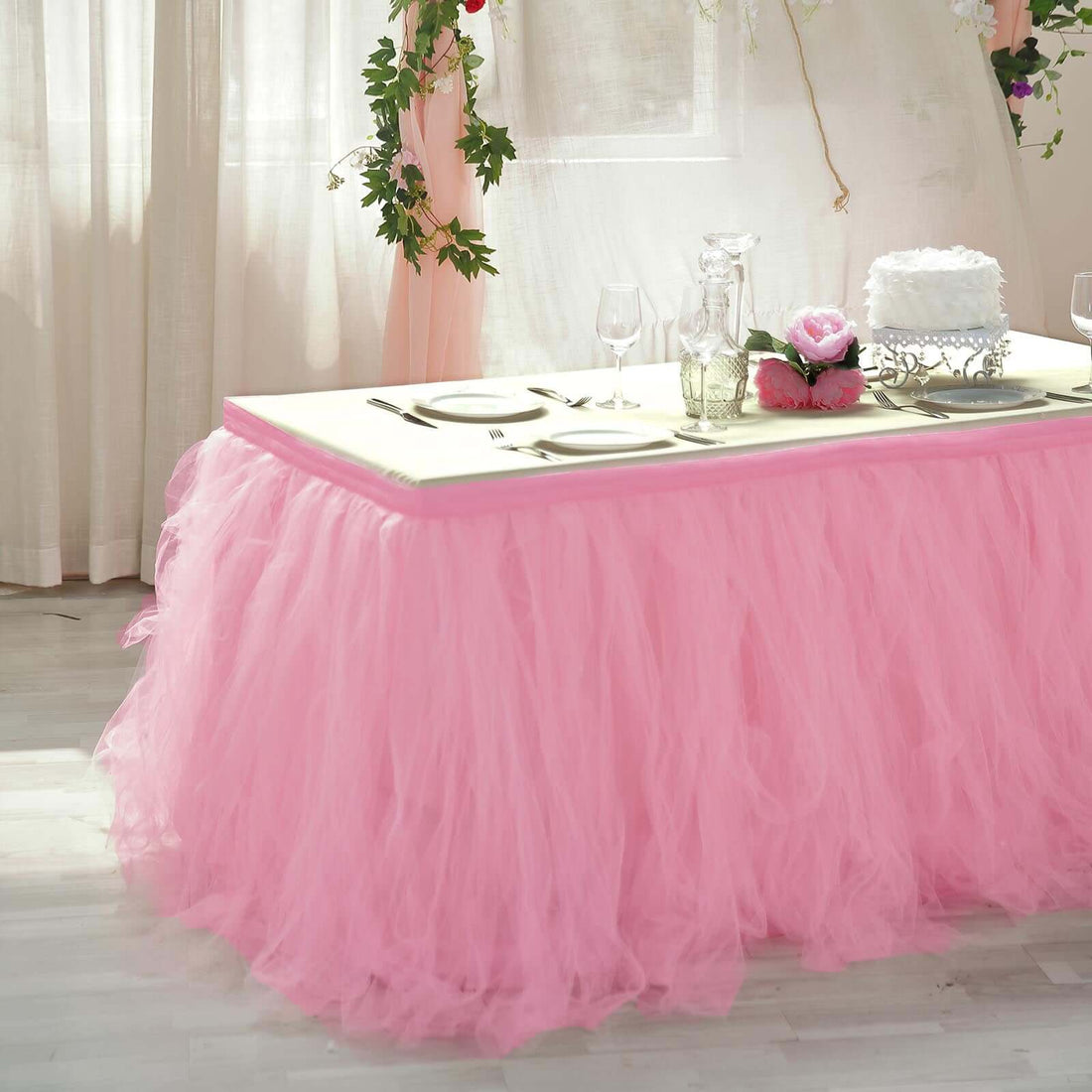 Pink tulle table skirt draping over a white table in a decorated setting.