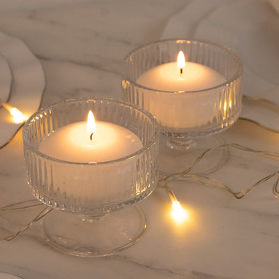Two lit candles in ribbed glass holders with warm fairy lights