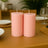 Pink pillar candles on a dining table with plates and greenery in the background.