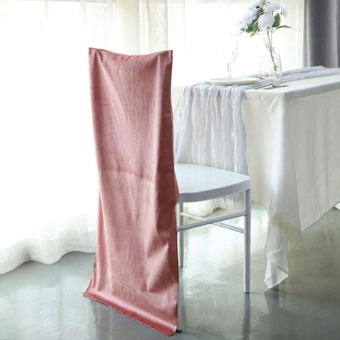 Elegant pink chair cover draped on a white chair in a bright dining setting.