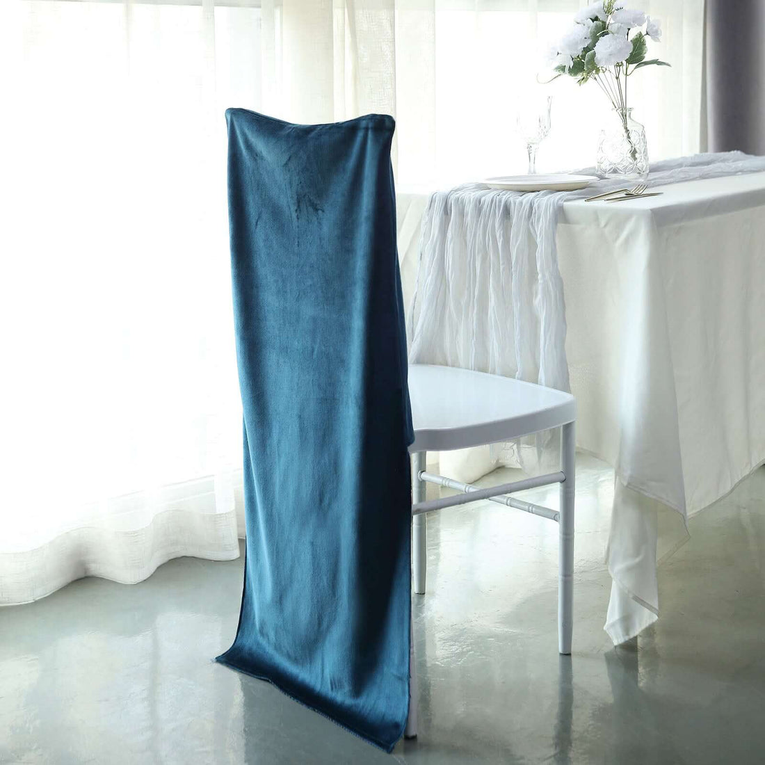 Elegant teal chair cover draped over a white chair in a bright dining setting.