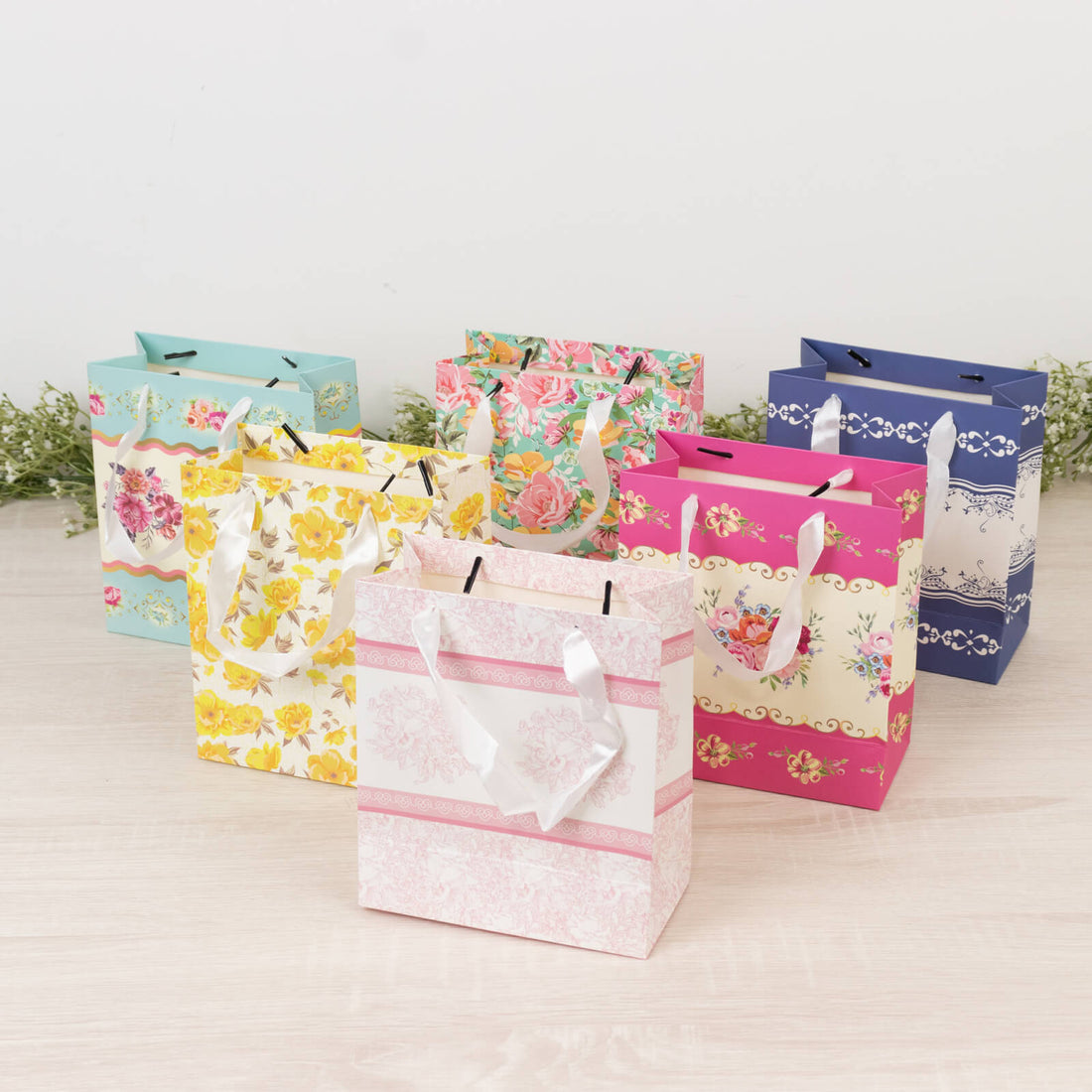 Colorful gift bags with floral designs on a light wooden surface.
