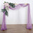 Purple wedding arch with floral arrangement and flowing drapes.