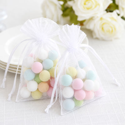 White organza gift bags with pastel candy balls on a soft floral background