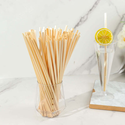 Natural bamboo straws in a clear glass vase on a marble countertop.