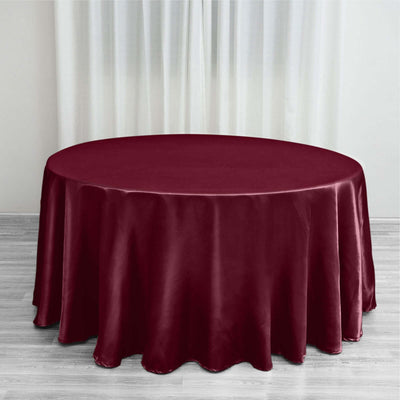 Burgundy round tablecloth on a wooden floor with sheer curtains.