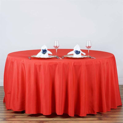 Red round tablecloth with white napkins and glasses set for dining.