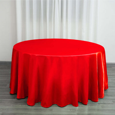 Red satin tablecloth draped over a round table in a bright setting.