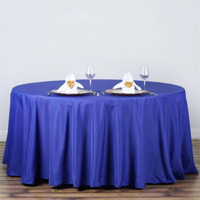 Round blue tablecloth draped over a table set for dining with glasses and napkin art.
