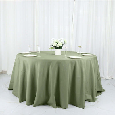 Round olive green tablecloth with elegant table setting and floral centerpiece.