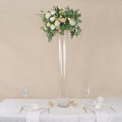 Tall glass vase with white and green floral arrangement on elegantly set dining table.