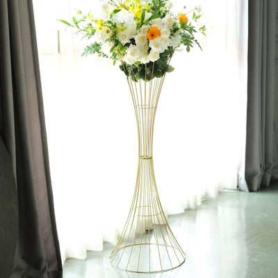 Gold wire vase with floral arrangement beside a window.
