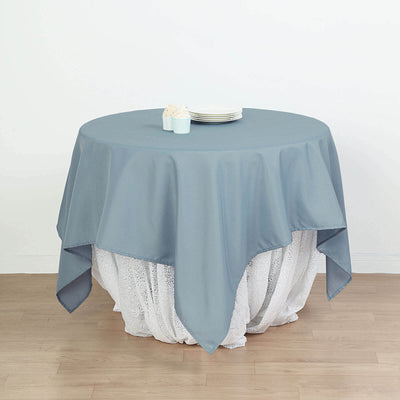 Round gray tablecloth draped over a white lace table skirt with plates on top.