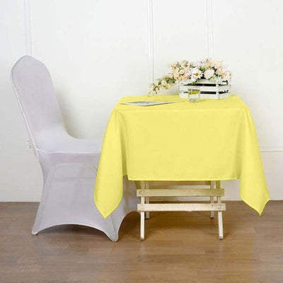 Yellow tablecloth draped over a wooden table with a clear chair and flowers.