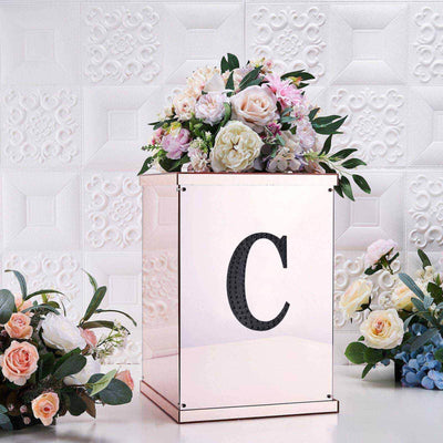 Elegant flower arrangement in a decorative box with a letter "C" on a textured background.