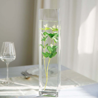 Tall glass vase with green leaves and water, elegantly displayed on a table.
