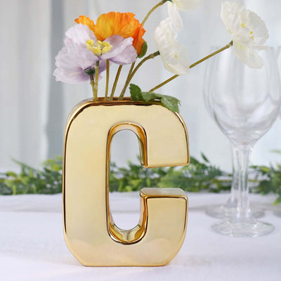 Gold letter 'G' vase with flowers, studio-style isolation shot.