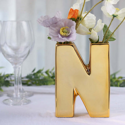 Gold letter "N" vase with flowers on a table.