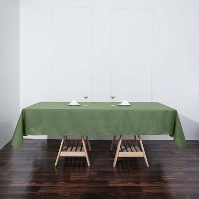 Green tablecloth on a wooden table set with glasses and napkins.