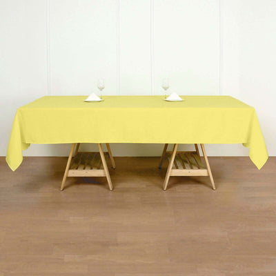 Yellow tablecloth on a wooden table set for dining with glasses and napkins.