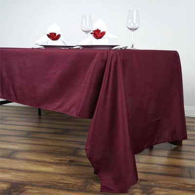 Elegant burgundy tablecloth draped on a dining table with wine glasses and napkins.