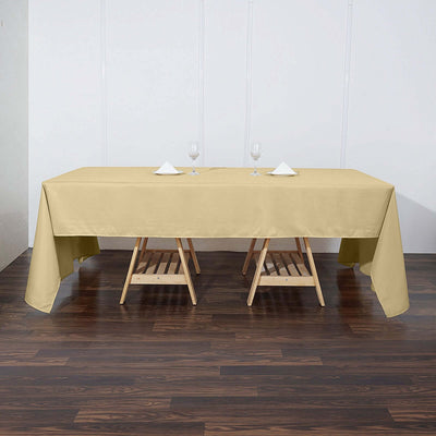 Beige tablecloth draped over two wooden tables with glasses and napkins.