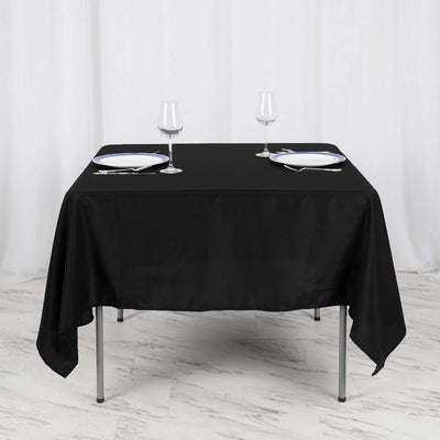 Black tablecloth draped over a table set for two with wine glasses and plates.