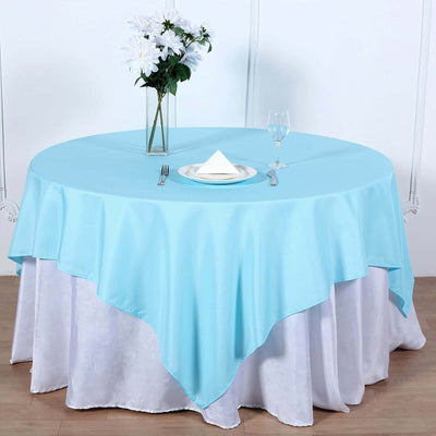 Round blue tablecloth draped over a white table with a glass and flowers