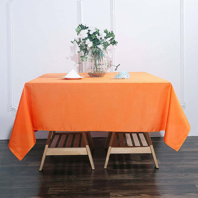 Orange tablecloth draped over a wooden table with floral arrangement.