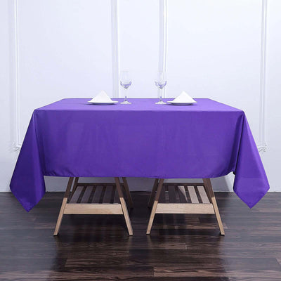 Purple tablecloth draped over a wooden table set with glasses and napkins.