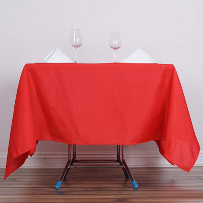 Red tablecloth draped over a folding table with wine glasses and napkins.