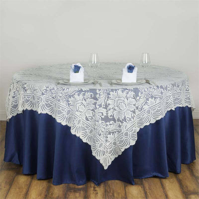White lace tablecloth on a round navy table with elegant place settings.