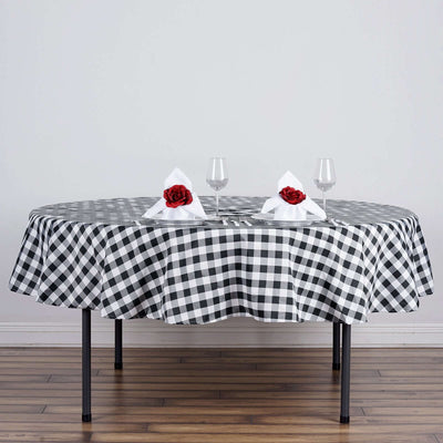 Round black and white checkered tablecloth set with rose-decorated napkins and wine glasses.