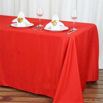 Red tablecloth set for dining with elegant napkin folds and wine glasses.