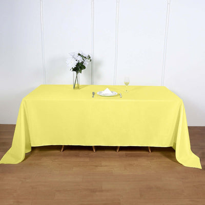 Yellow tablecloth draped over a wooden table with a vase and glass.