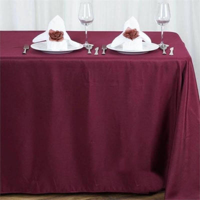 Elegant burgundy tablecloth set for dining with rose-themed napkins and glassware.